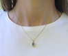 Woman wearing a 1 carat Oval Blue Sapphire and Diamond Halo Pendant in 14k yellow gold